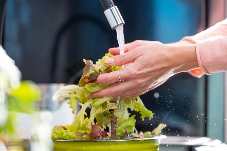 A person washing lettuce in a sink