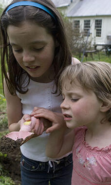 two girls in garden looking at worm