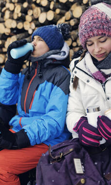 3 teens in winter gear, drinking from water bottles, looking at phone