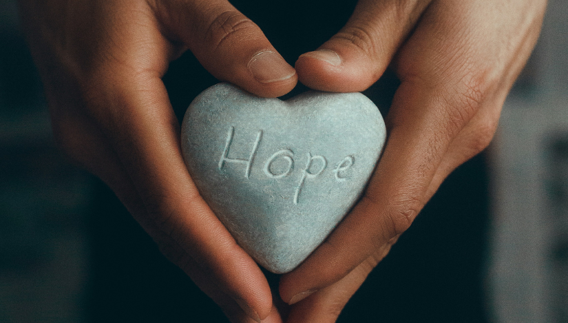 Hands holding stone with the word Hope engraved in it
