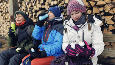 3 teens in winter gear, drinking from water bottles, looking at phone